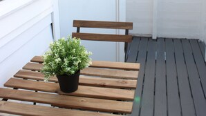 Un banco de madera con una planta en maceta en un balcón con paredes y ventanas blancas.
