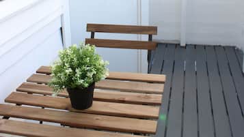 A wooden bench with a potted plant on a balcony with white walls and windows.