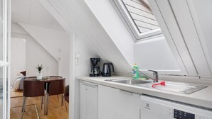 Una cocina moderna con tragaluz, armarios blancos, cafetera y pileta.