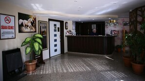 A reception area with a reception desk, a sign prohibiting smoking, a framed picture of a horse, and a potted plant. - Otel Familia (Orhangazi)