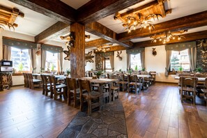 Un restaurante con mesas y sillas de madera, suelo de piedra y cornamentas de ciervo en las paredes.