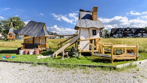 A playground with wooden structures, including a slide and climbing area, set in a grassy field with houses in the background. - Dworek Mysliwski Hubert (Bukowina Tatrzanska)