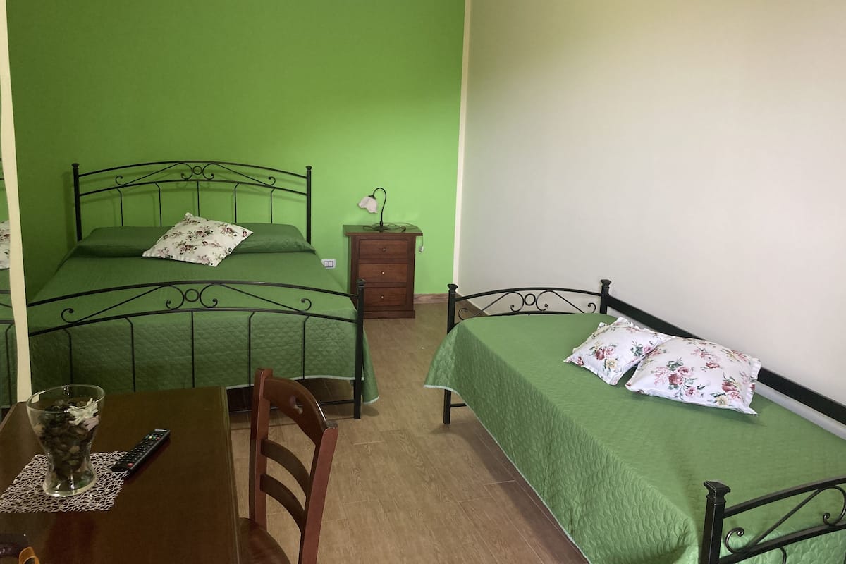 A room with two beds, a wooden table with a remote control, and a chair.