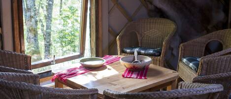 Una habitación acogedora con muebles de mimbre, una mesa de madera y un ventanal con vistas a un bosque.