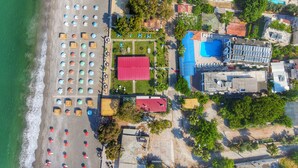 Vista aerea di una zona costiera con spiaggia, ombrelloni e un edificio dal tetto rosso.