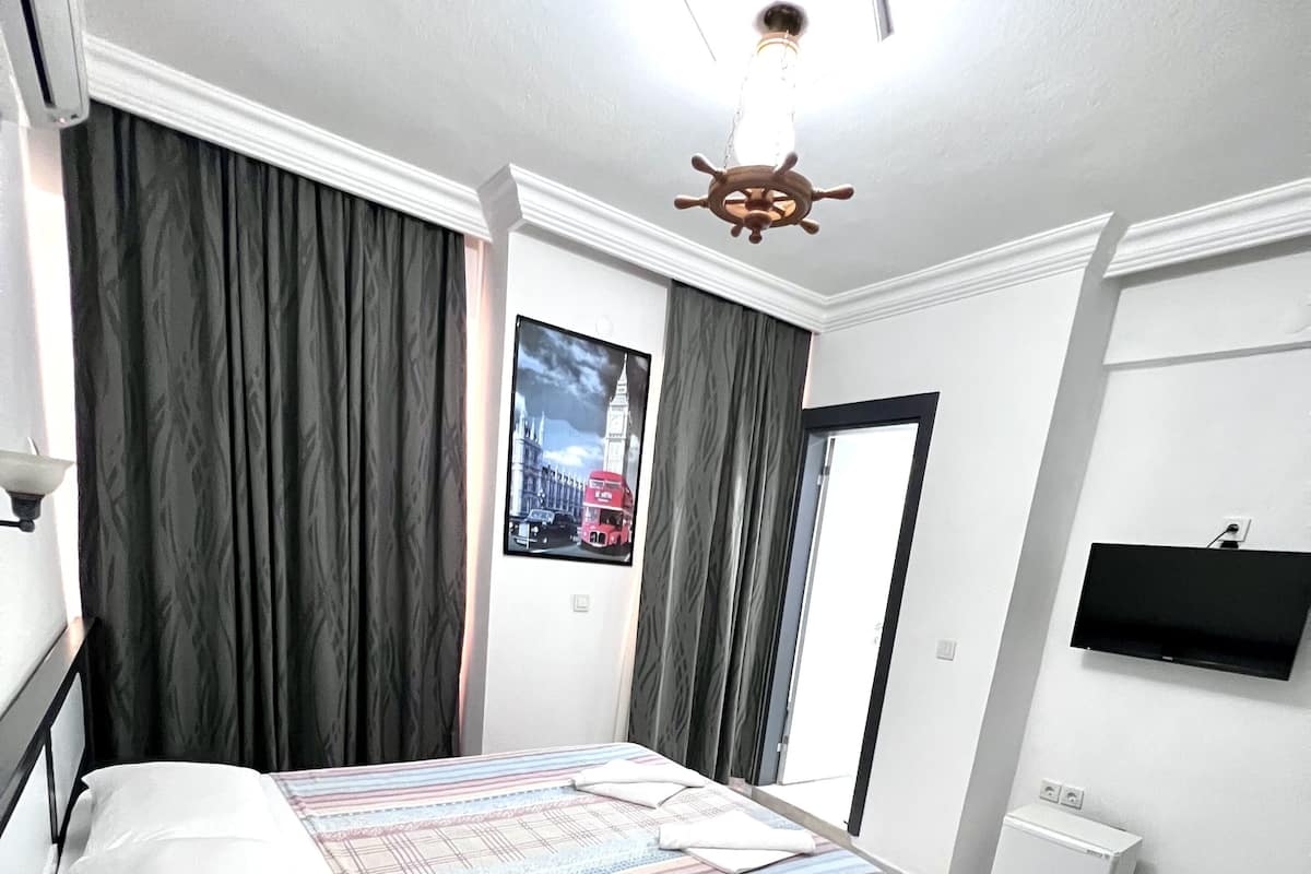 A bedroom with a bed, a flat-screen TV, a ceiling fan, and a window with curtains.