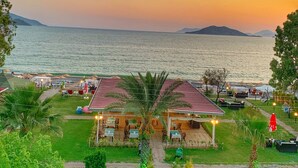 Un ristorante sul mare con posti a sedere all'aperto, un giardino e vista mare e colline in lontananza.