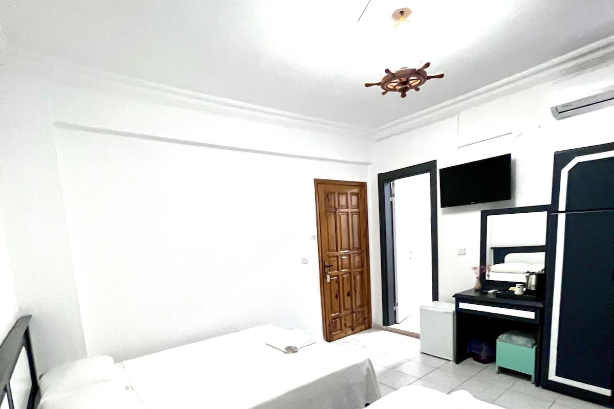 A hotel room with two single beds, a wooden door, a small desk with a chair, a television, and a wardrobe.