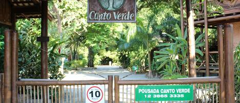 A wooden gate with a sign that reads "Pousada Canto Verde" and a speed limit sign of 10 km/h.
