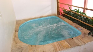 A small, rectangular hot tub with a wooden border, situated in a corner of a room with a white wall and a red door. - Pousada Canto Verde (São Sebastião)
