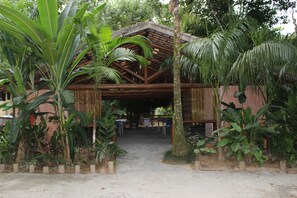 Une construction rustique en bois, dotée d’un toit de chaume, entourée d’une végétation tropicale luxuriante.