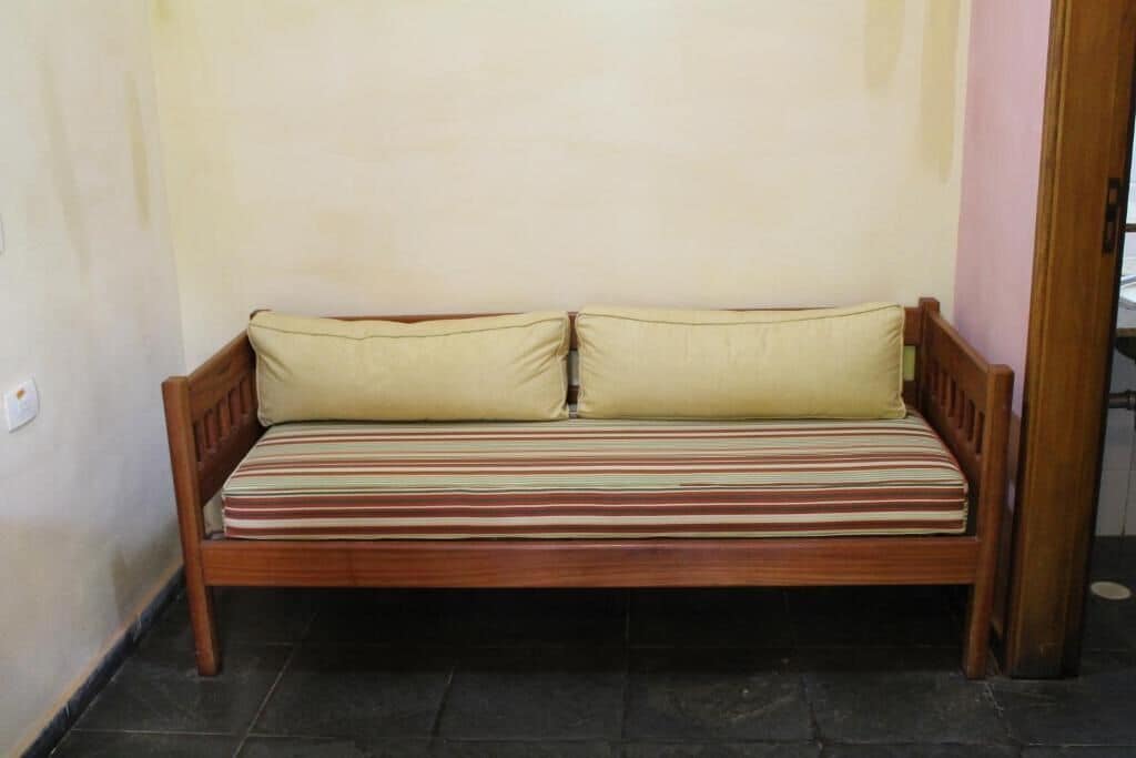 A wooden bench with a striped cushion against a plain wall.