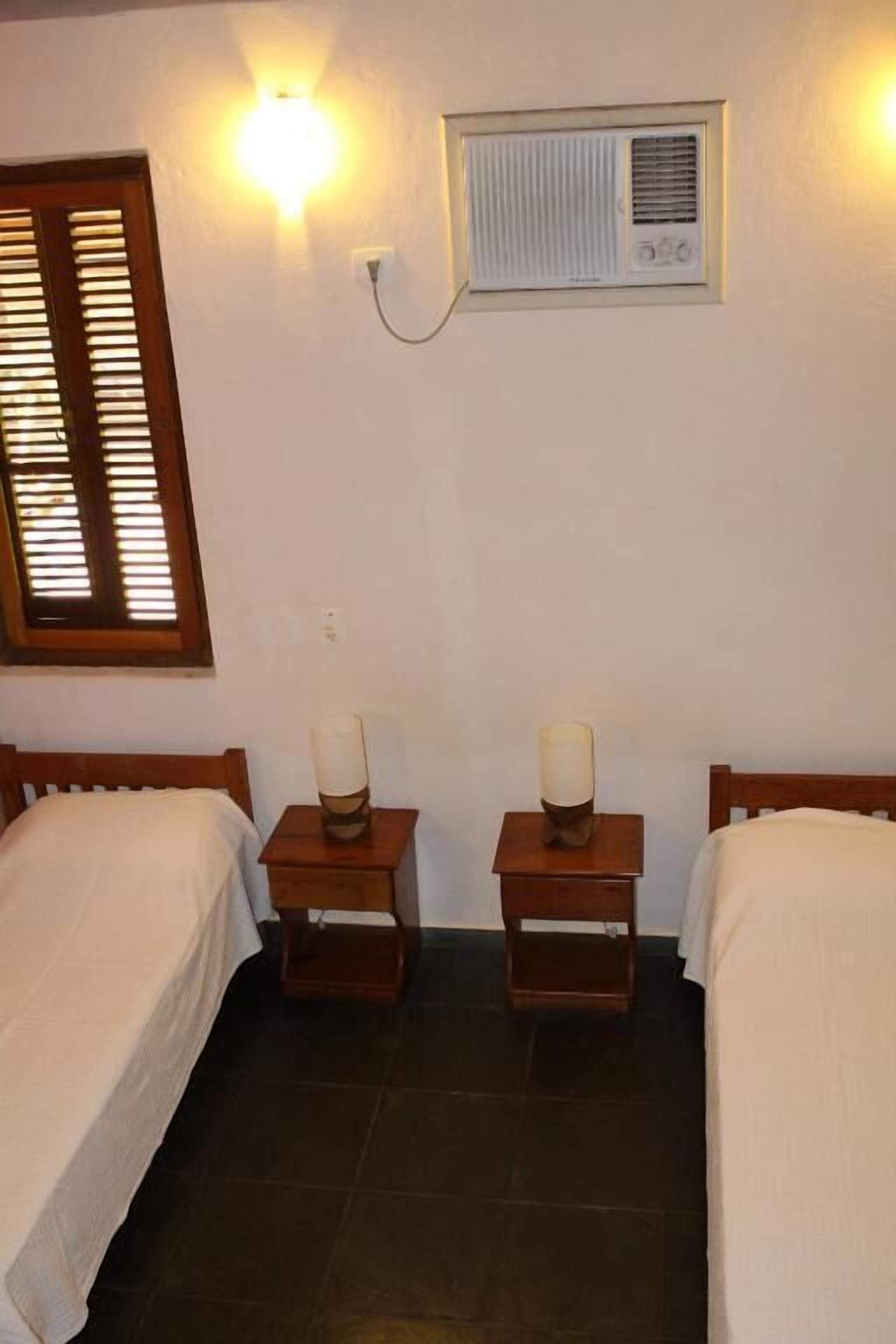 A room with two single beds, a wall-mounted air conditioner, and bedside lamps.
