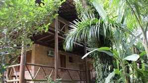 A rustic wooden structure with a brick exterior, surrounded by lush greenery and a palm tree. - Pousada Canto Verde (São Sebastião)