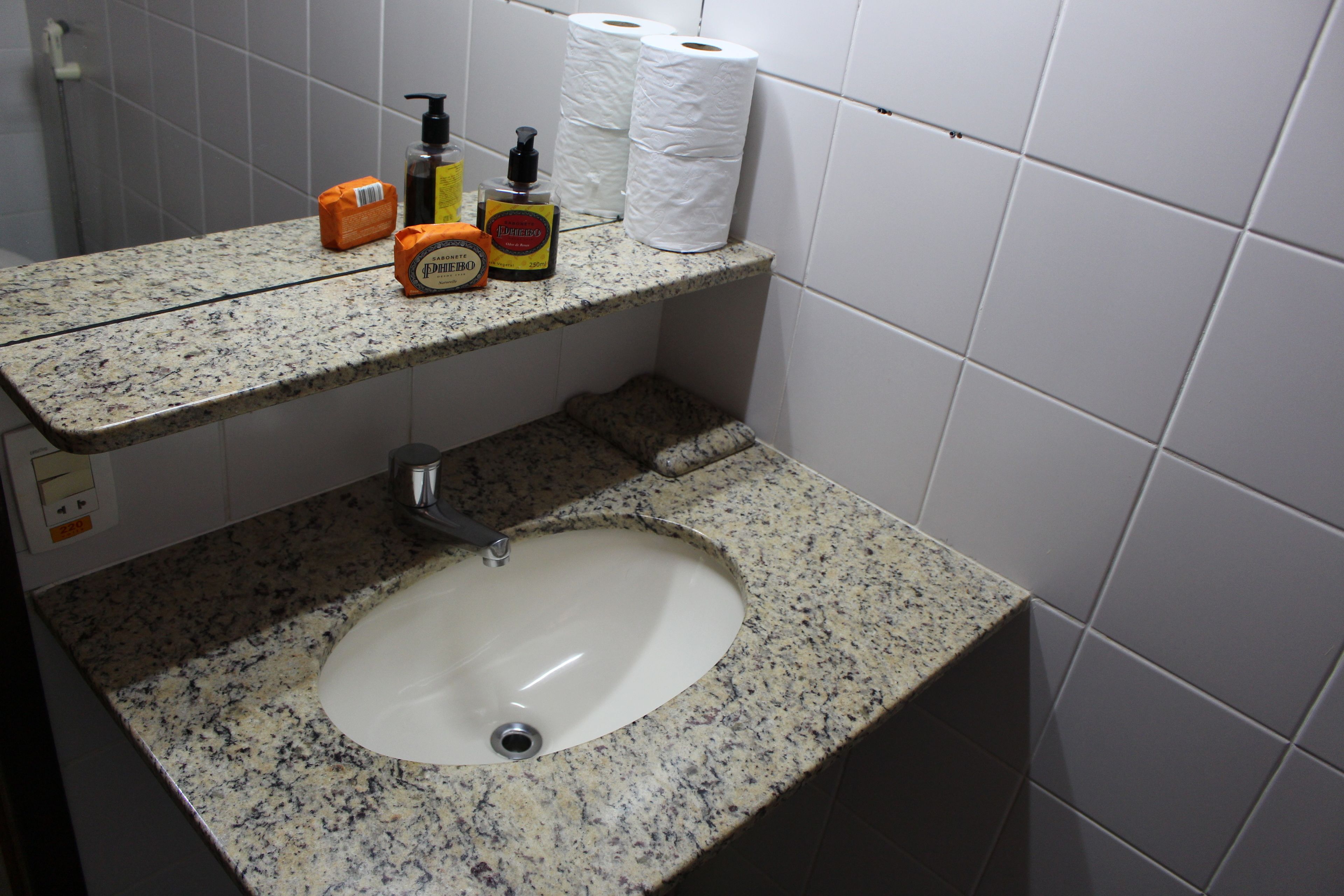 A bathroom with a granite countertop, a sink, and toiletries including a soap dispenser, a bottle of hand sanitizer, and toilet paper.