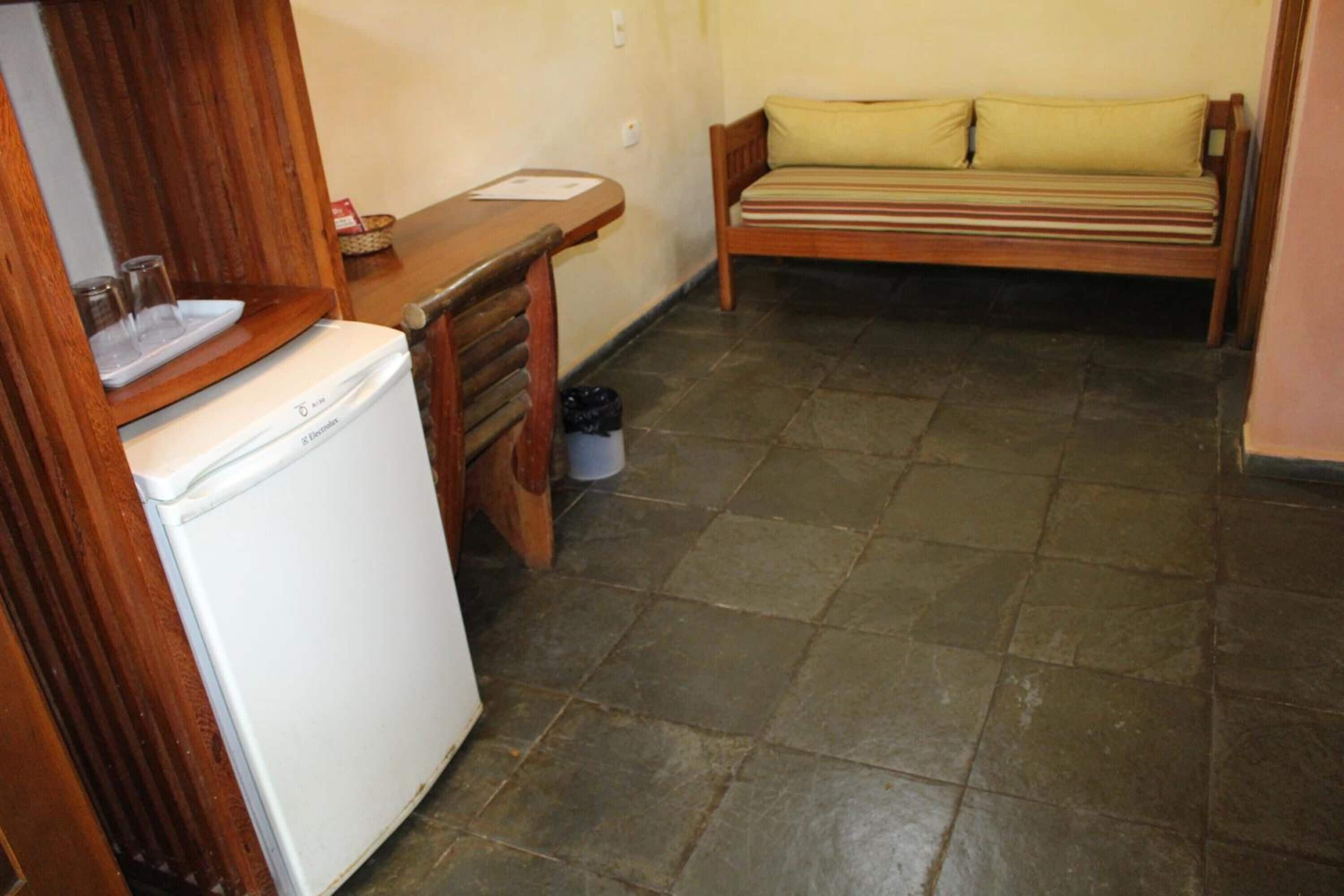 A compact kitchen with a refrigerator, wooden counter, and a bench with cushions.