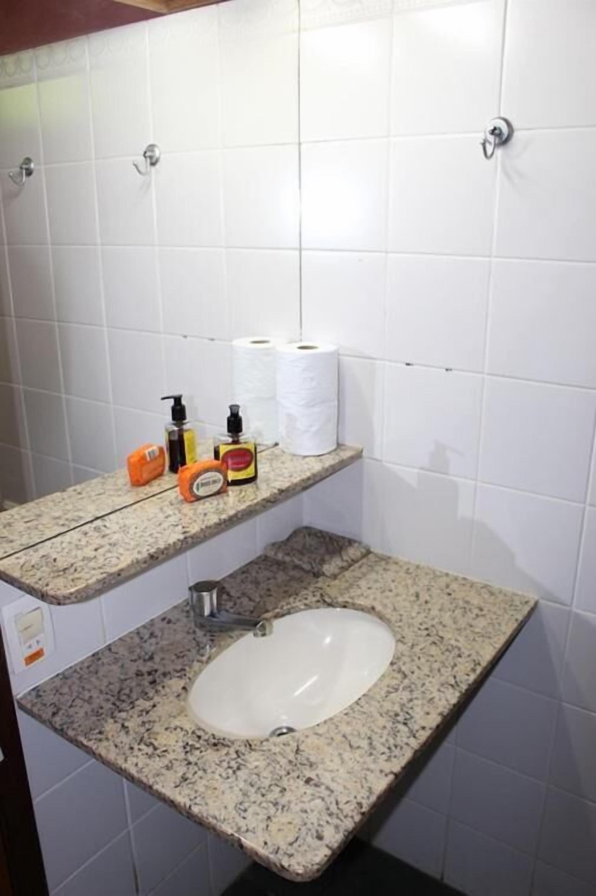 Een badkamer met witte betegelde wanden, een granieten aanrecht, een wastafel en een plank met toiletartikelen.