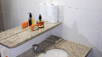 Een badkamer met witte betegelde wanden, een granieten aanrecht, een wastafel en een plank met toiletartikelen.