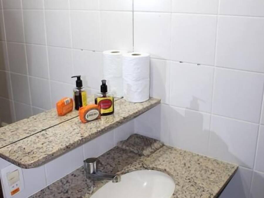 Een badkamer met witte betegelde wanden, een granieten aanrecht, een wastafel en een plank met toiletartikelen.