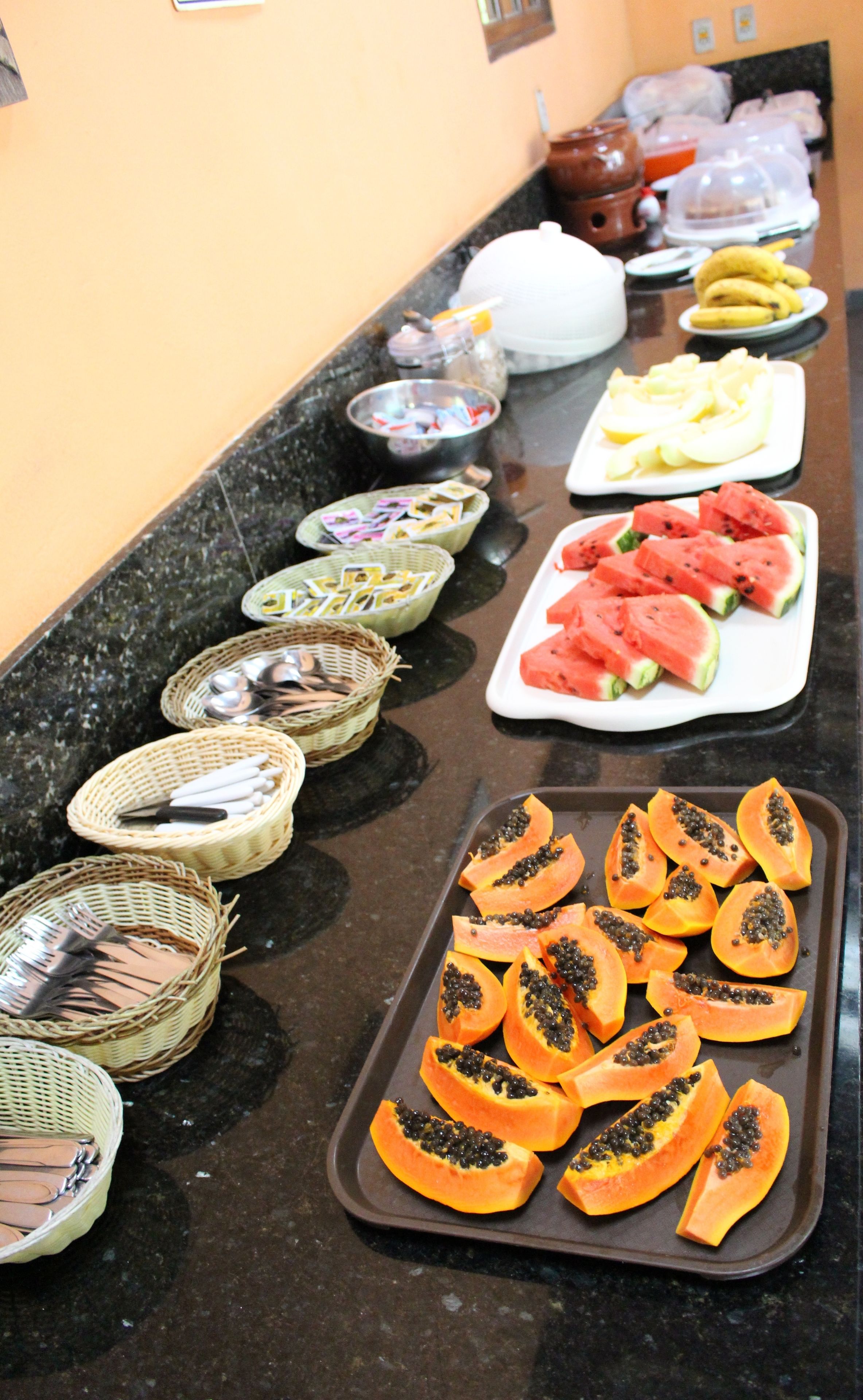 A buffet table with various food items including sliced watermelon, papaya, and bananas.
