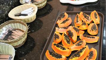 A buffet table with various food items including sliced watermelon, papaya, and bananas.