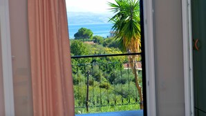 Un balcon offrant une vue sur un paysage côtier, avec notamment un palmier et une chaîne de montagnes à l’horizon.