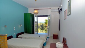 Une chambre avec deux lits, une armoire verte, une table en bois et une vue sur l’extérieur.