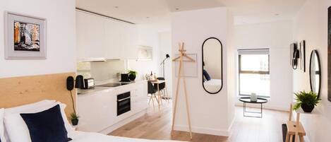 Quarto de hotel moderno com uma cama grande, uma kitchenette, um espaço de refeições e vista para a cidade.