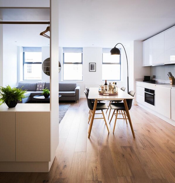 A modern kitchen with white cabinets, a dining table with chairs, and a black pendant light. - Hiding Space - Westgate Apartments (Bath)