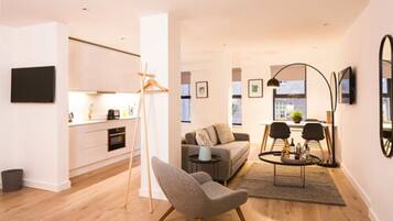 A modern living room with a sofa, armchair, coffee table, and a dining area with chairs.