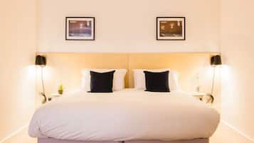 A double bed with white bedding, two black pillows, and a light-colored headboard. There are two framed pictures on the wall above the bed.