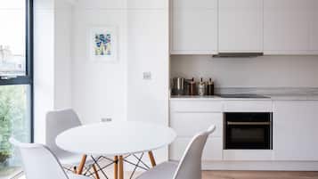 Een moderne keuken met witte kastjes, een inbouwoven en een eetgedeelte met een ronde tafel en witte stoelen.