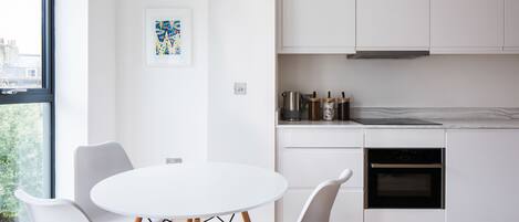 A modern kitchen with white cabinets, a built-in oven, and a dining area with a round table and white chairs.