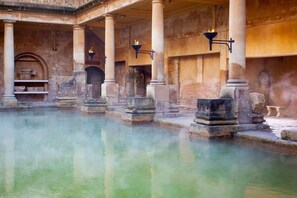 Un edificio histórico con una piscina central, columnas de piedra y puertas abovedadas.