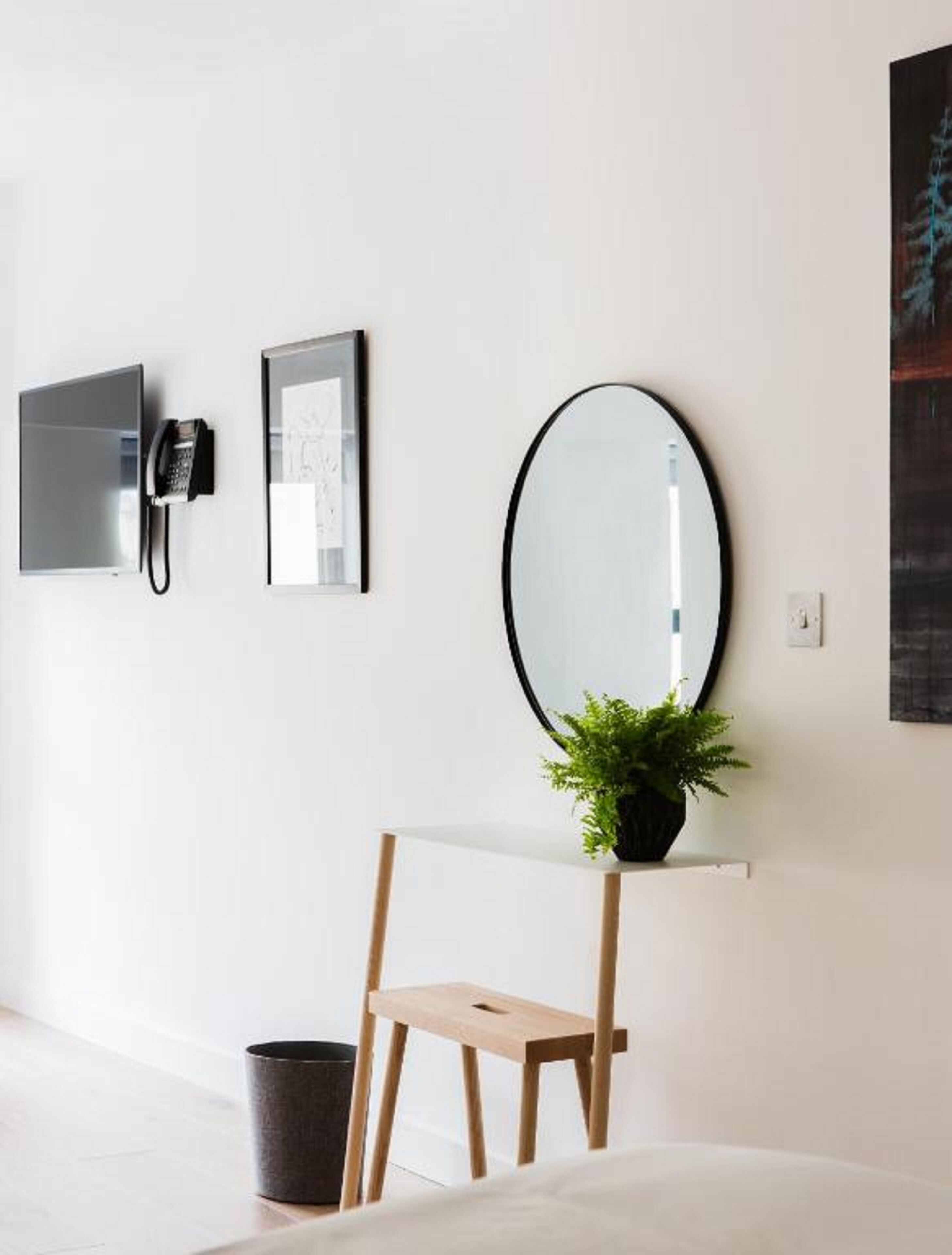 A minimalist room with a desk, a telephone, a framed picture, a mirror, and a potted plant.