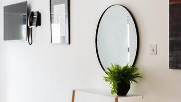 A minimalist room with a desk, a telephone, a framed picture, a mirror, and a potted plant.