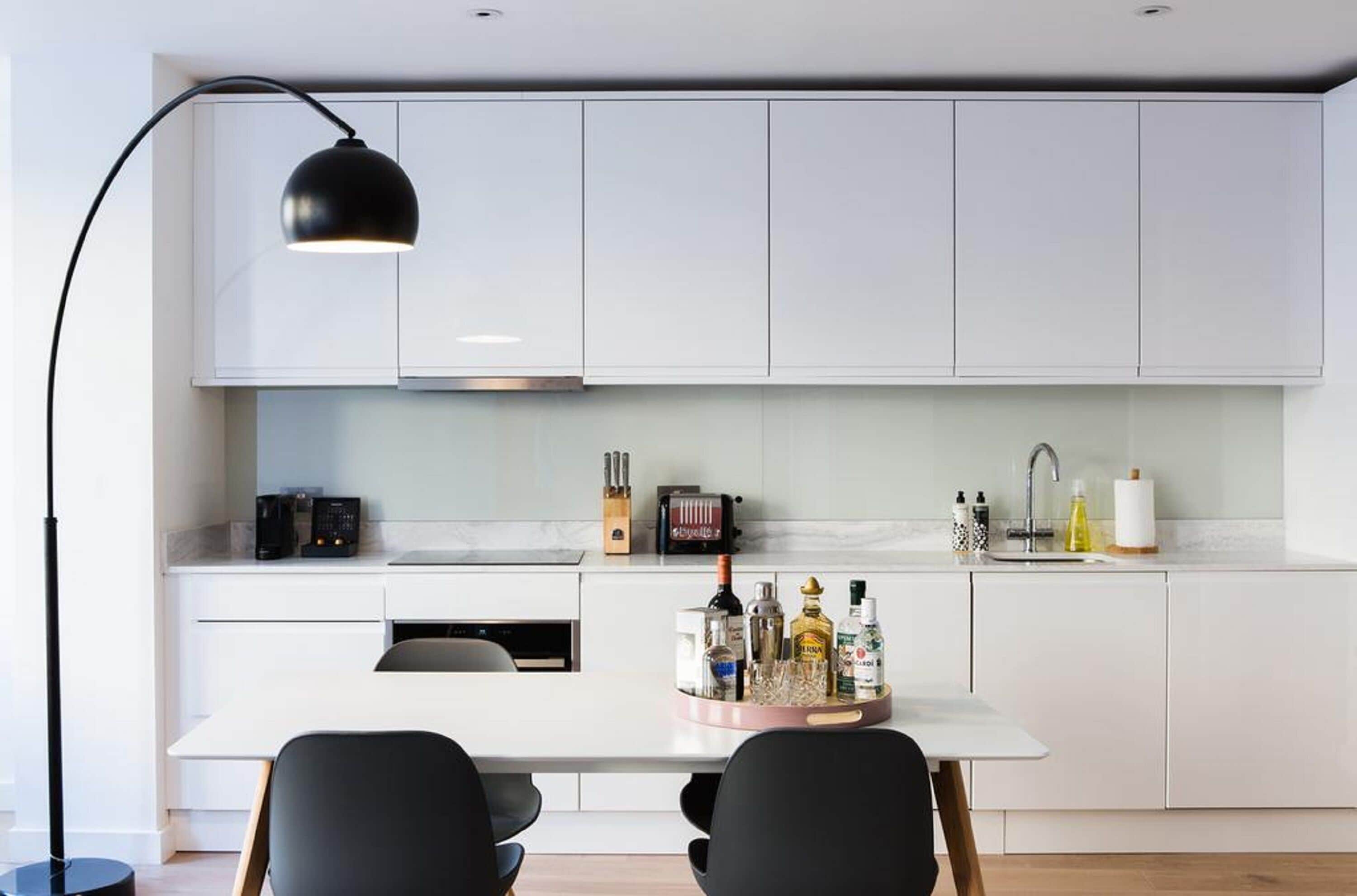 A modern kitchen with white cabinets, a black pendant light, and a table with chairs.
