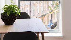 Ein Zimmer mit Fenster und Blick auf die Stadtlandschaft, einem Tisch mit Topfpflanze und einem Stuhl.