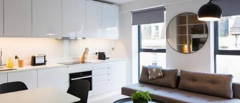 Una cocina moderna con armarios blancos, un comedor con mesa y sillas, y una sala de estar con sofá y una mesa redonda de centro.