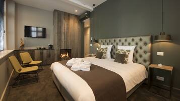 Une chambre d’hôtel moderne dotée d’un grand lit, d’une cheminée, d’une télévision et d’un coin salon avec des fauteuils.