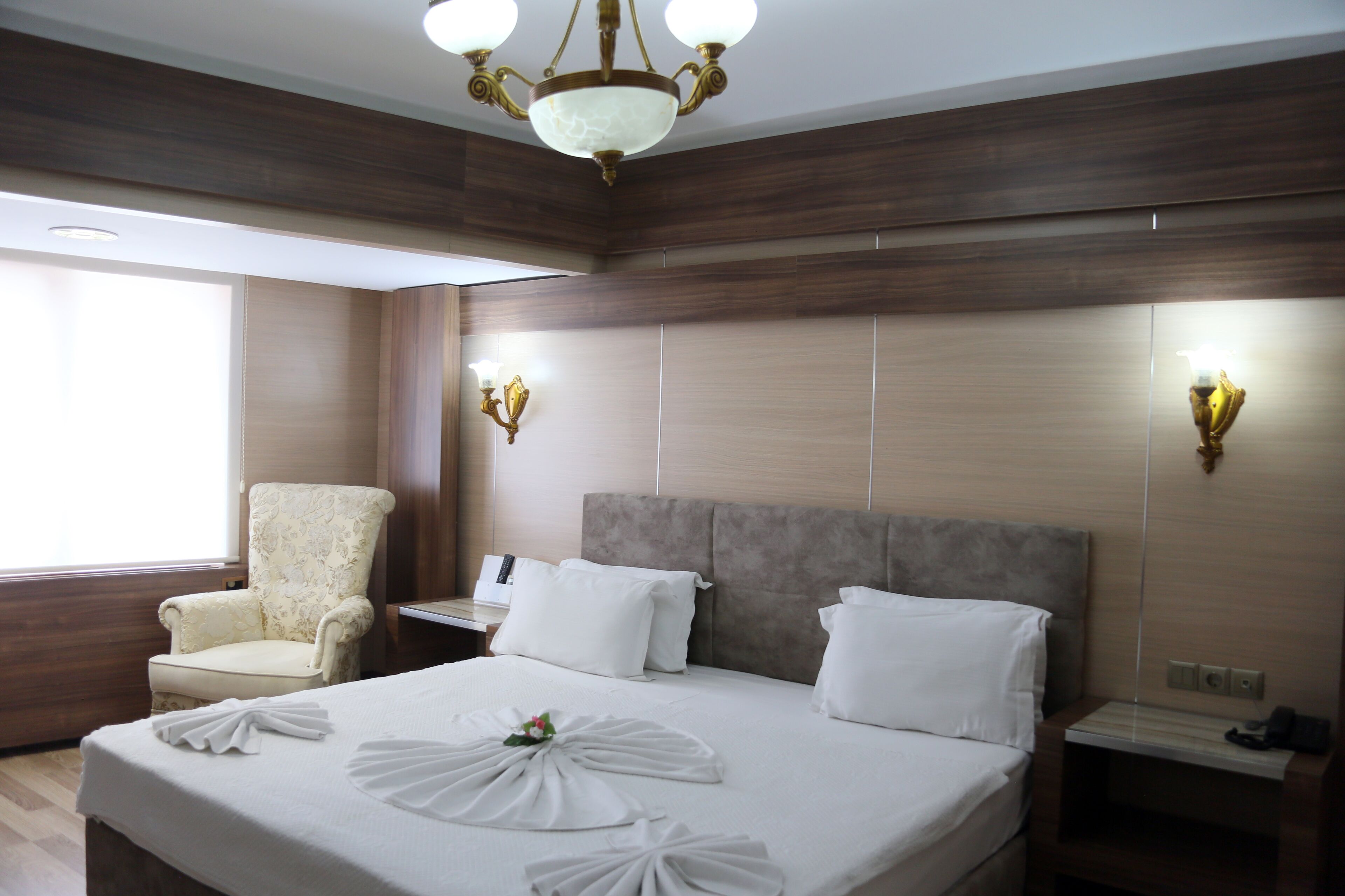 Habitación de hotel con una cama grande, una silla, una mesita de noche y una lámpara en la pared.