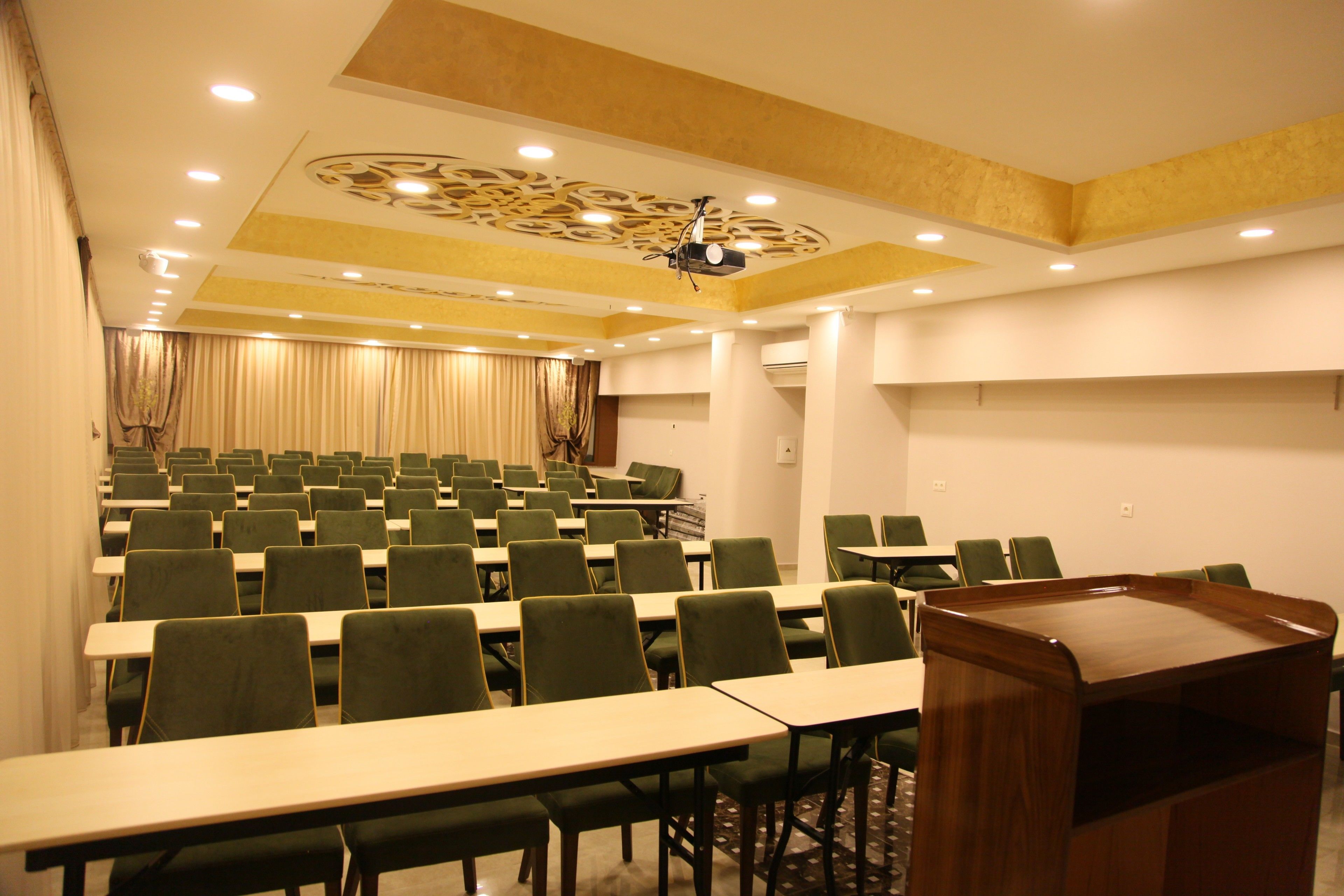A conference room with rows of green chairs, a podium, and a stage with curtains.