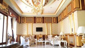 Un salon luxueux, agrémenté d’un lustre, de meubles élégants et d’un téléviseur à écran plat fixé au mur.
