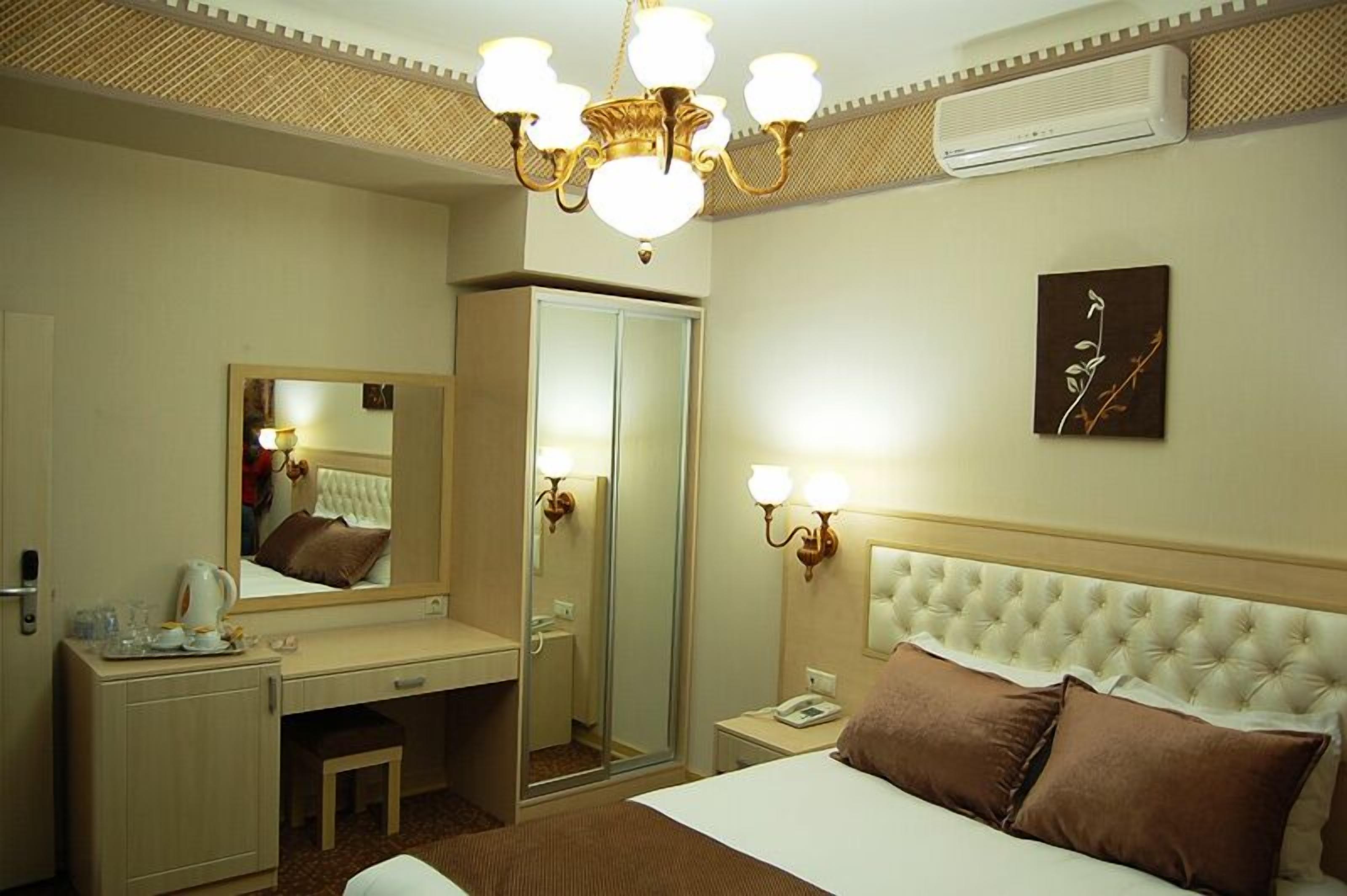 Une chambre d’hôtel comprenant un lit, un bureau, un miroir, une table de chevet avec une lampe et un climatiseur fixé au mur.