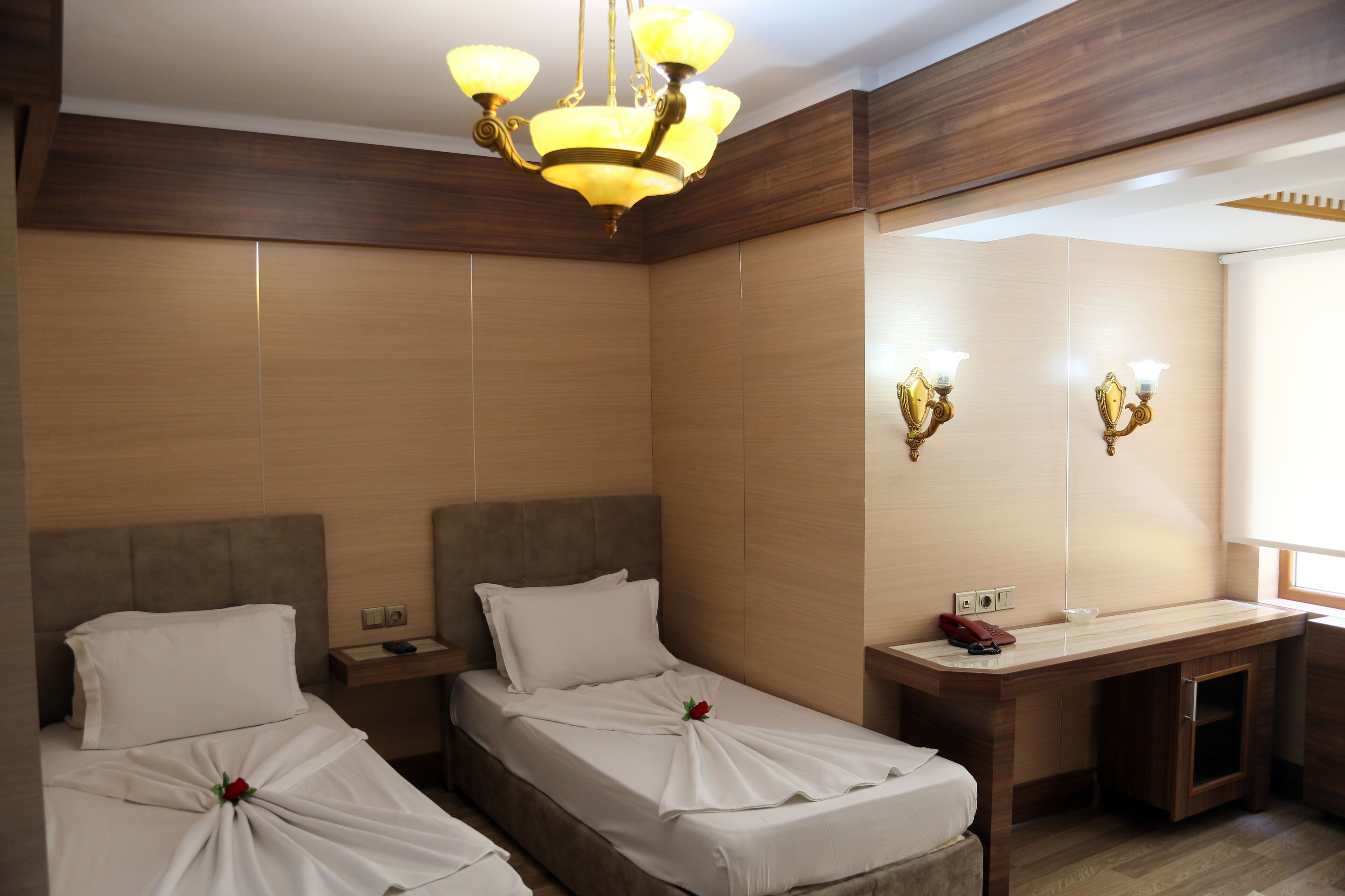 A hotel room with two beds, a desk, a mirror, and a chandelier.