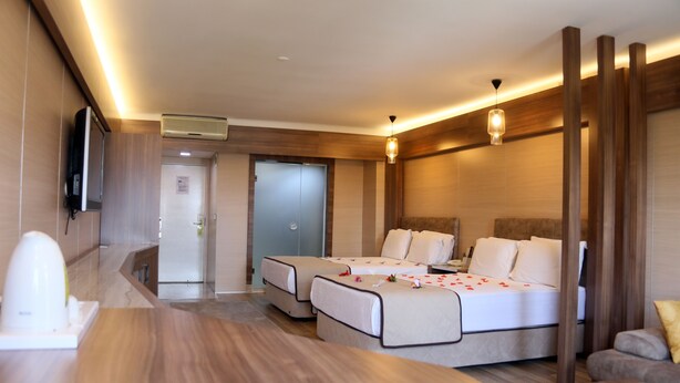 Une chambre d’hôtel moderne avec un plancher en bois, un lit recouvert d’une courtepointe blanche, un canapé et un téléviseur à écran plat fixé au mur.