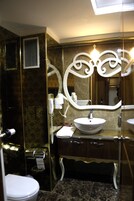 Un baño con pared de mármol, un lavabo blanco, un mueble de tocador con cajones, un espejo y un inodoro.