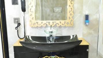 Uma casa de banho com toucador preto, lavatório de vidro, espelho com moldura decorativa, telefone e dispensador de sabonete.