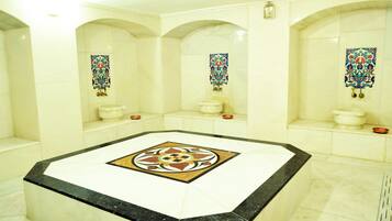 Bathroom features a central square floor with a geometric pattern, three arched niches with pedestal sinks and decorative tiles above.
