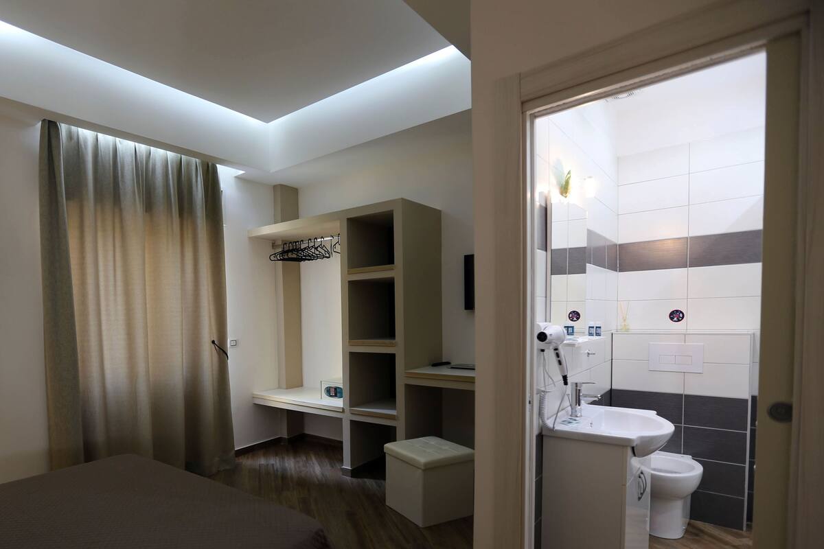 Una habitación de hotel con cama, escritorio, armario y baño con inodoro y lavabo.